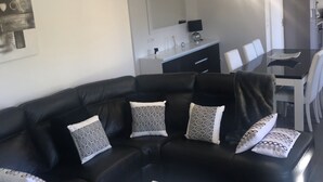 Ein modernes Wohnzimmer mit einer schwarzen Ledersofa, einem weißen Couchtisch und einem Essbereich im Hintergrund.