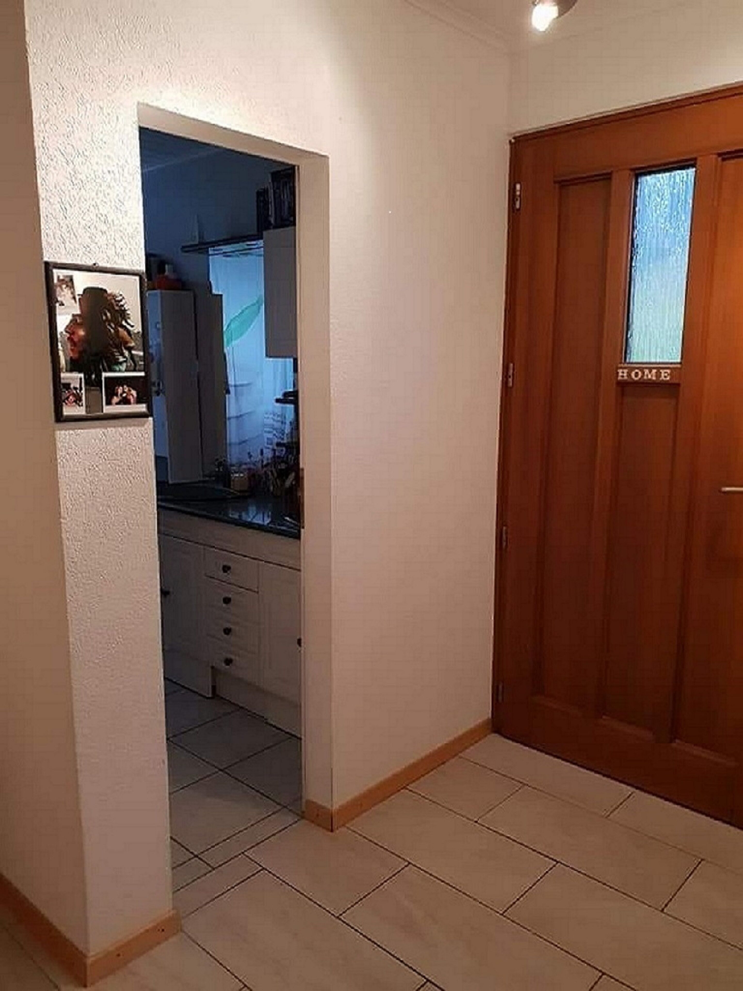 A hallway with a wooden door labeled "HOME" and a kitchen area visible through an open doorway.