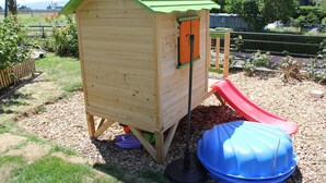 A wooden playhouse with a green roof and a red slide. - Chez Minnie (La Grande-Béroche)