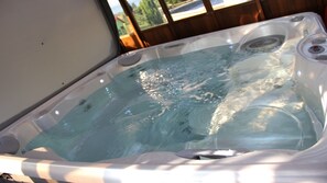 A hot tub with a clear view of the water, a control panel, and a window in the background.