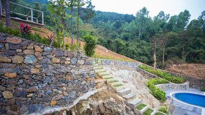 Un muro de piedra con escalones que conducen a una zona de piscina rodeada de abundante vegetación y un paisaje montañoso boscoso.