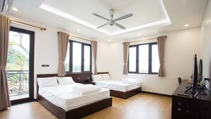 Habitación de hotel con dos camas, ventilador de techo y ventanas amplias con cortinas.