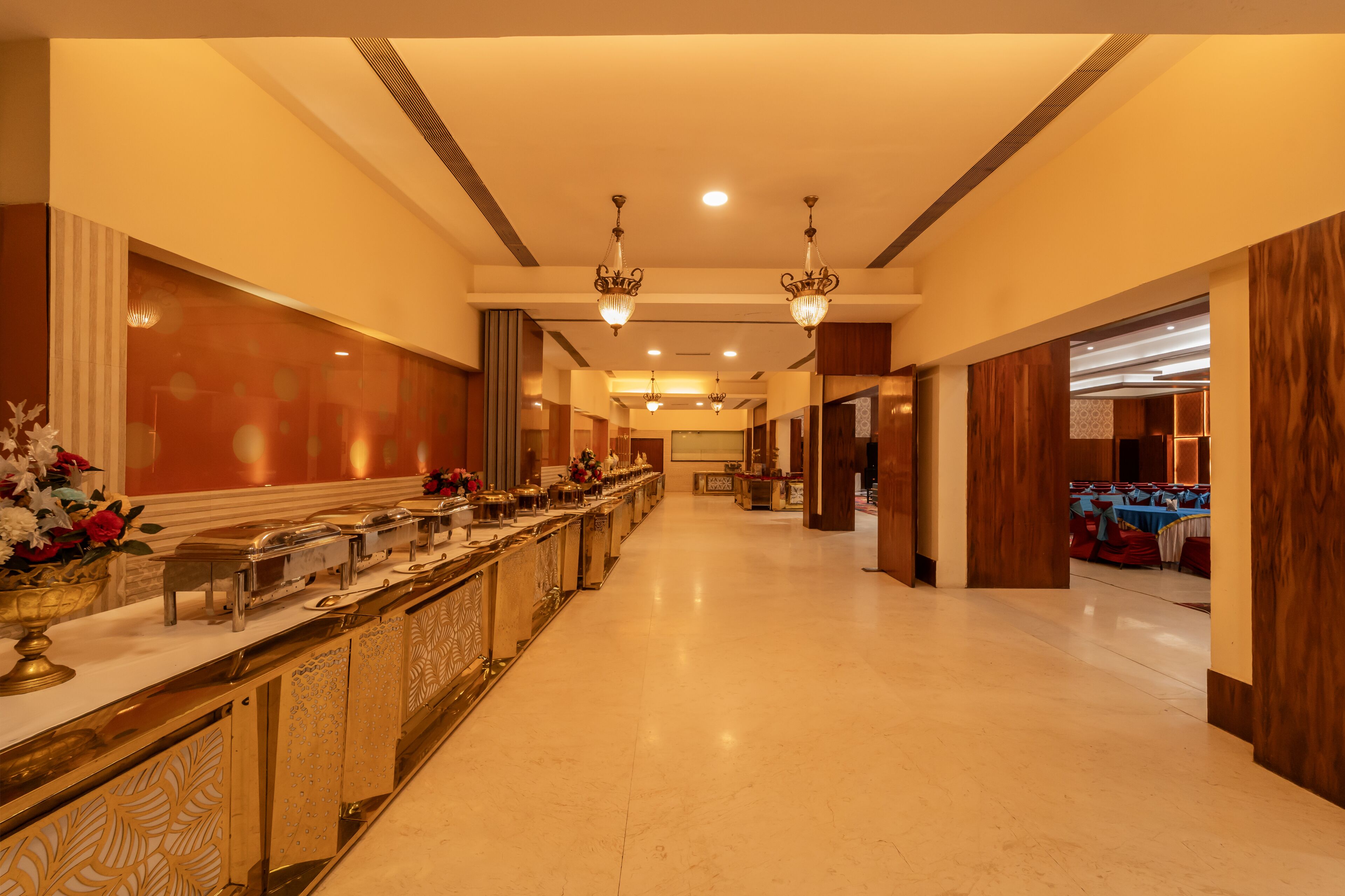 A hotel lobby with a long reception desk, chandeliers, and a view into a banquet area.