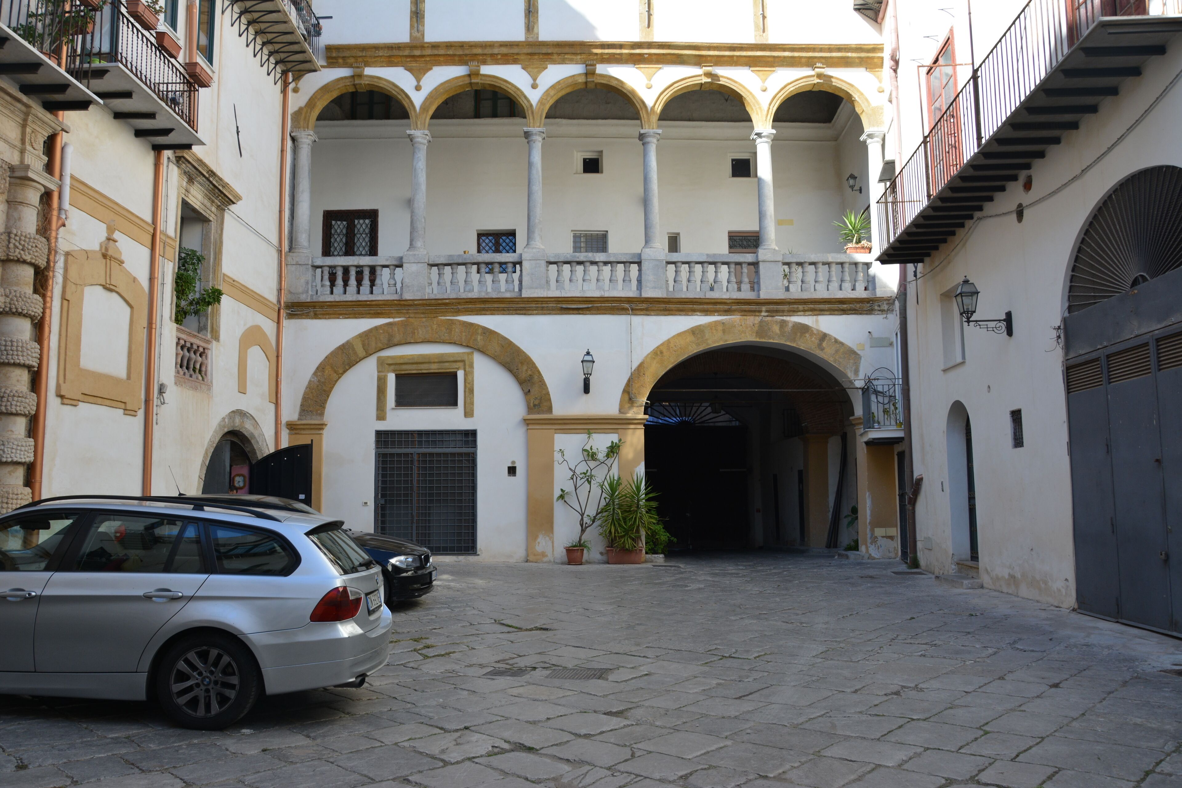 A courtyard with a car parked in front, a building with arches and balconies, and a gate.