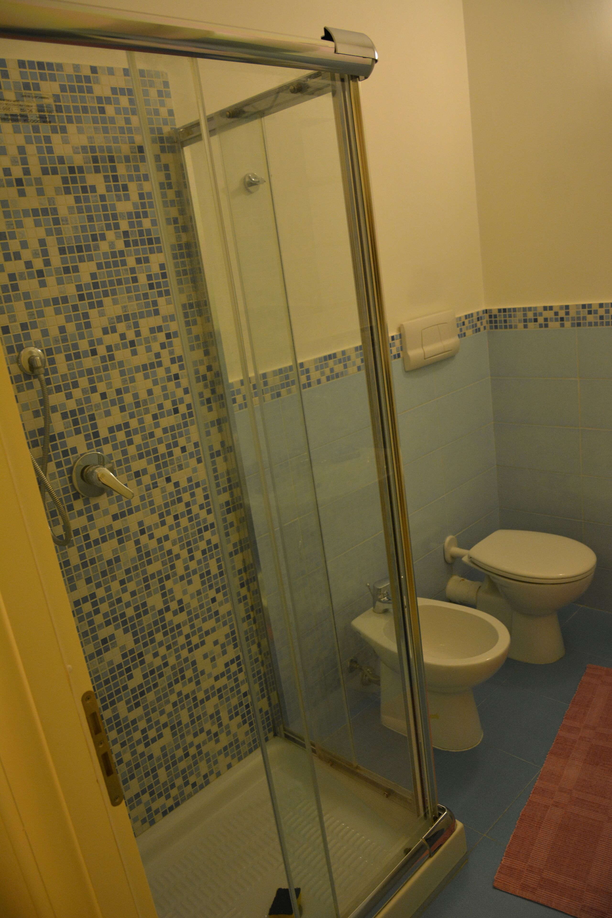A bathroom with a shower, two toilets, and a tiled floor.