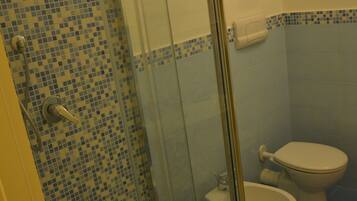A bathroom with a shower, two toilets, and a tiled floor.