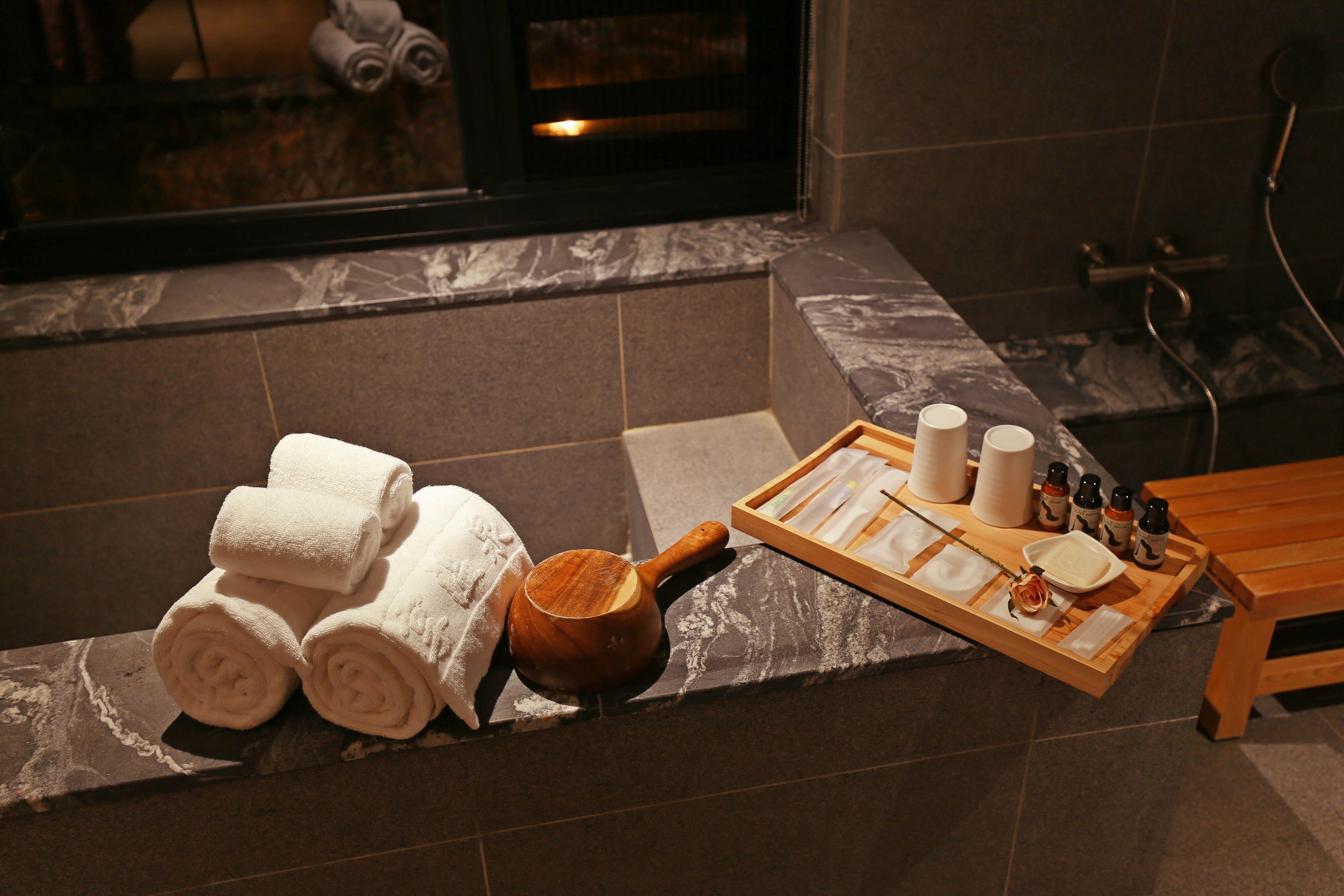 A bathroom with a bathtub, towels, a tray with toiletries, and a wooden bowl.