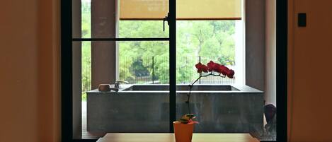 Una habitación minimalista con una mesa de madera, una planta en maceta y vistas a través de un gran ventanal.