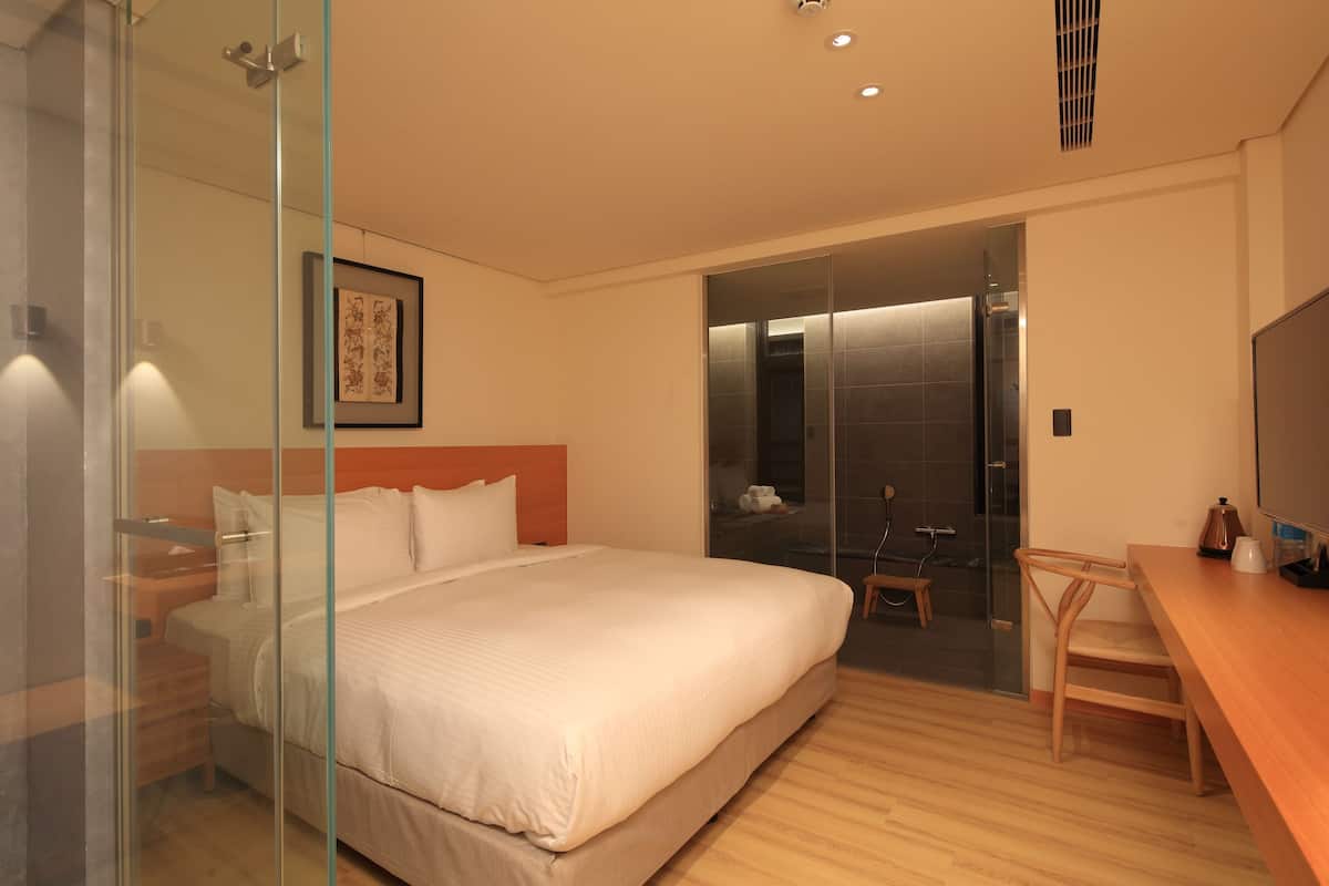 A modern hotel room with a large bed, a desk, and a glass shower enclosure.