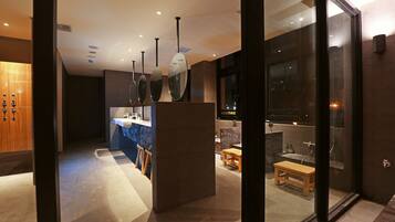 A modern bathroom with a glass partition, a wooden bench, and a sink area.