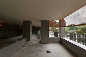 Een ruim balkon met uitzicht op de omgeving, met een stenen vloer en een metalen hekwerk.