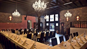 Une vaste salle de banquet avec de longues tables dressées pour le repas, des lustres et des murs en pierre.