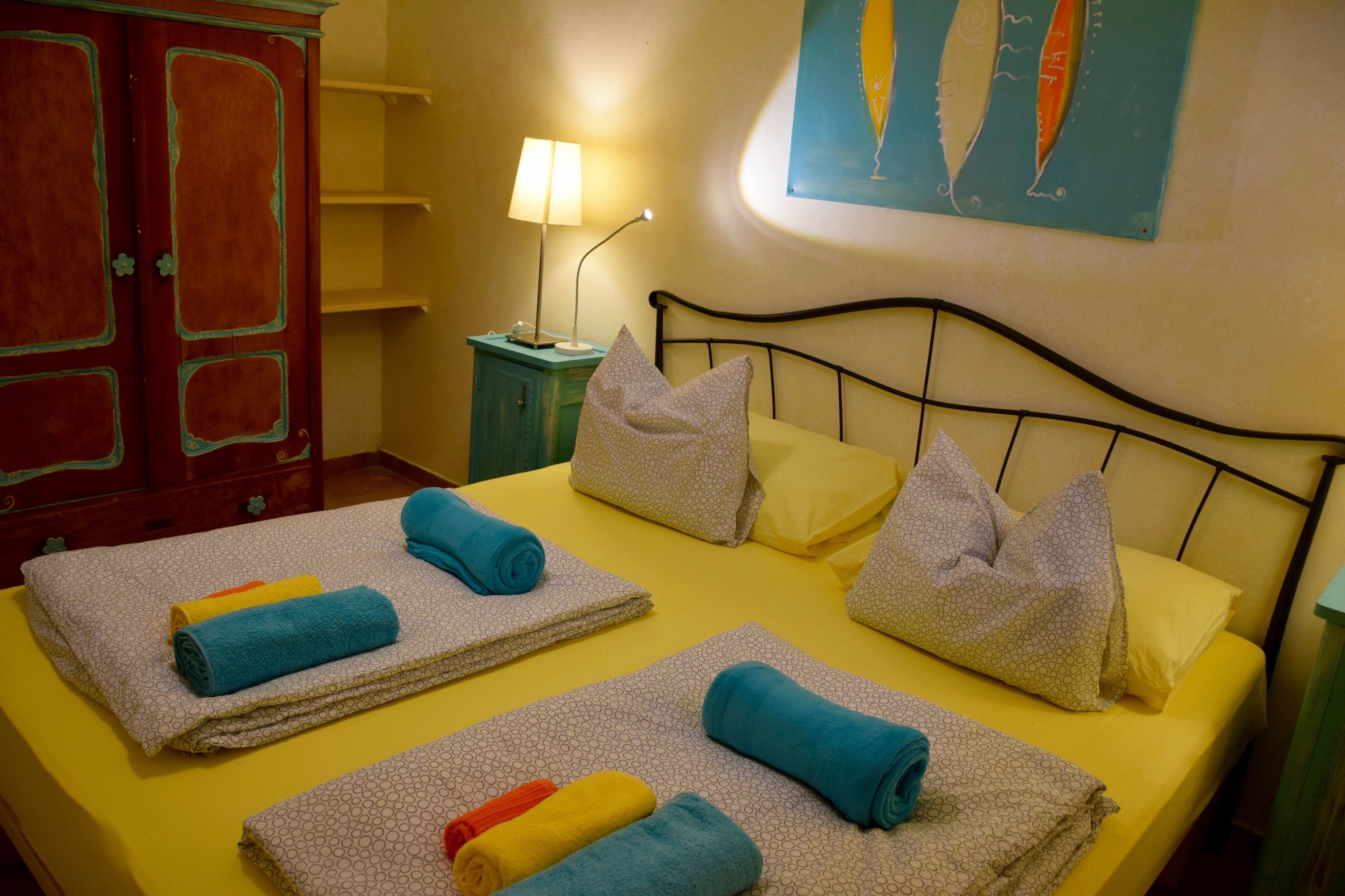Un lit bien fait, agrémenté de plusieurs serviettes et d’oreillers, une lampe de chevet et un tableau au mur.