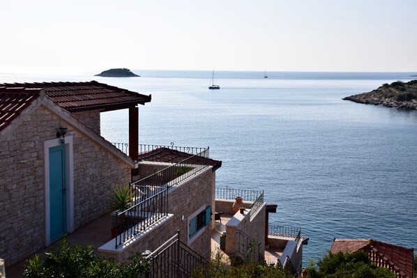 A stone building with a blue door, a balcony, and a view of the sea with boats.
