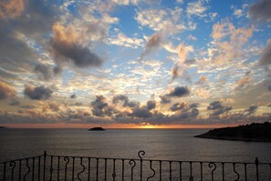 A sunset over the sea with a metal railing in the foreground.