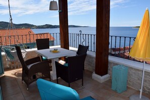 A balcony with a table and chairs, a hanging chair, and a view of the sea.