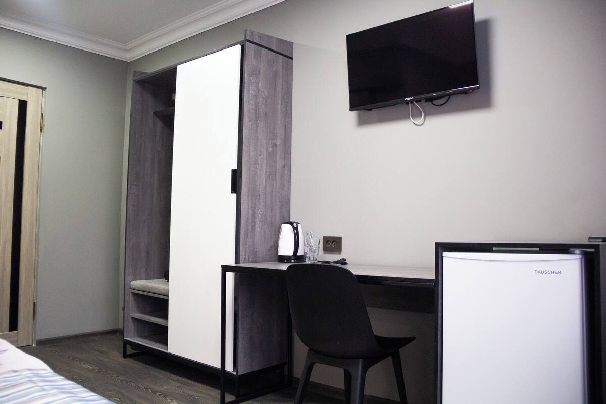 Una habitación de hotel pequeña con cama, escritorio con silla, televisor y un mini bar.