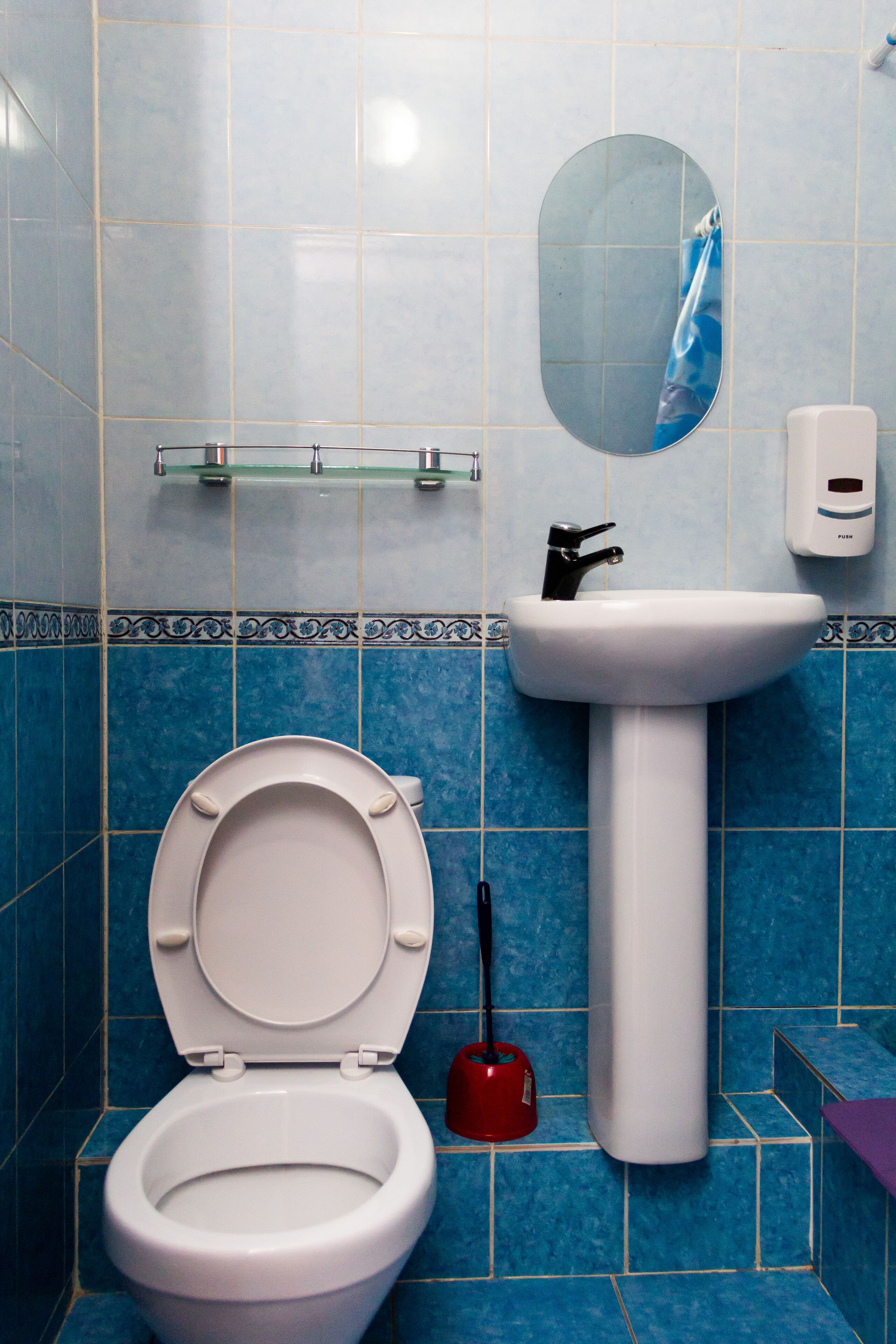 A bathroom with a white toilet, a white sink, a mirror, and a red plunger.