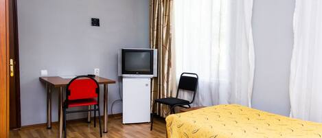 A hotel room with a bed, a desk with a chair, a television, and a window with curtains.