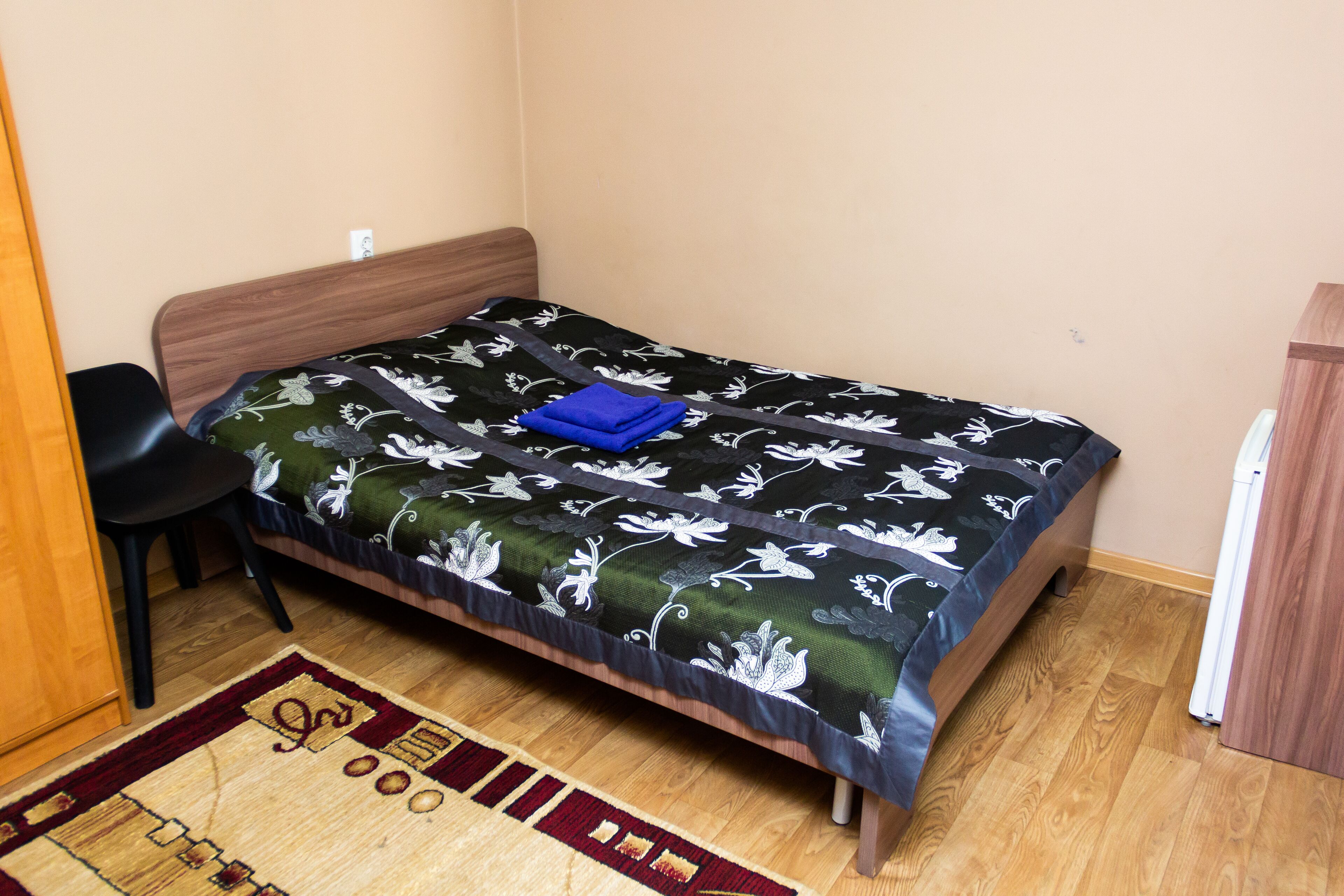 A small, neatly arranged bedroom with a single bed, a chair, and a wooden wardrobe.