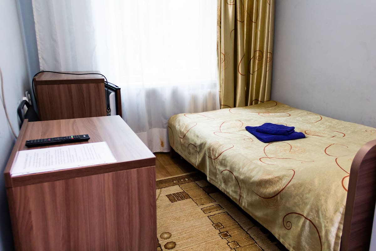 Una habitación de hotel con un escritorio de madera, una cama con edredón estampado y una ventana con cortinas.