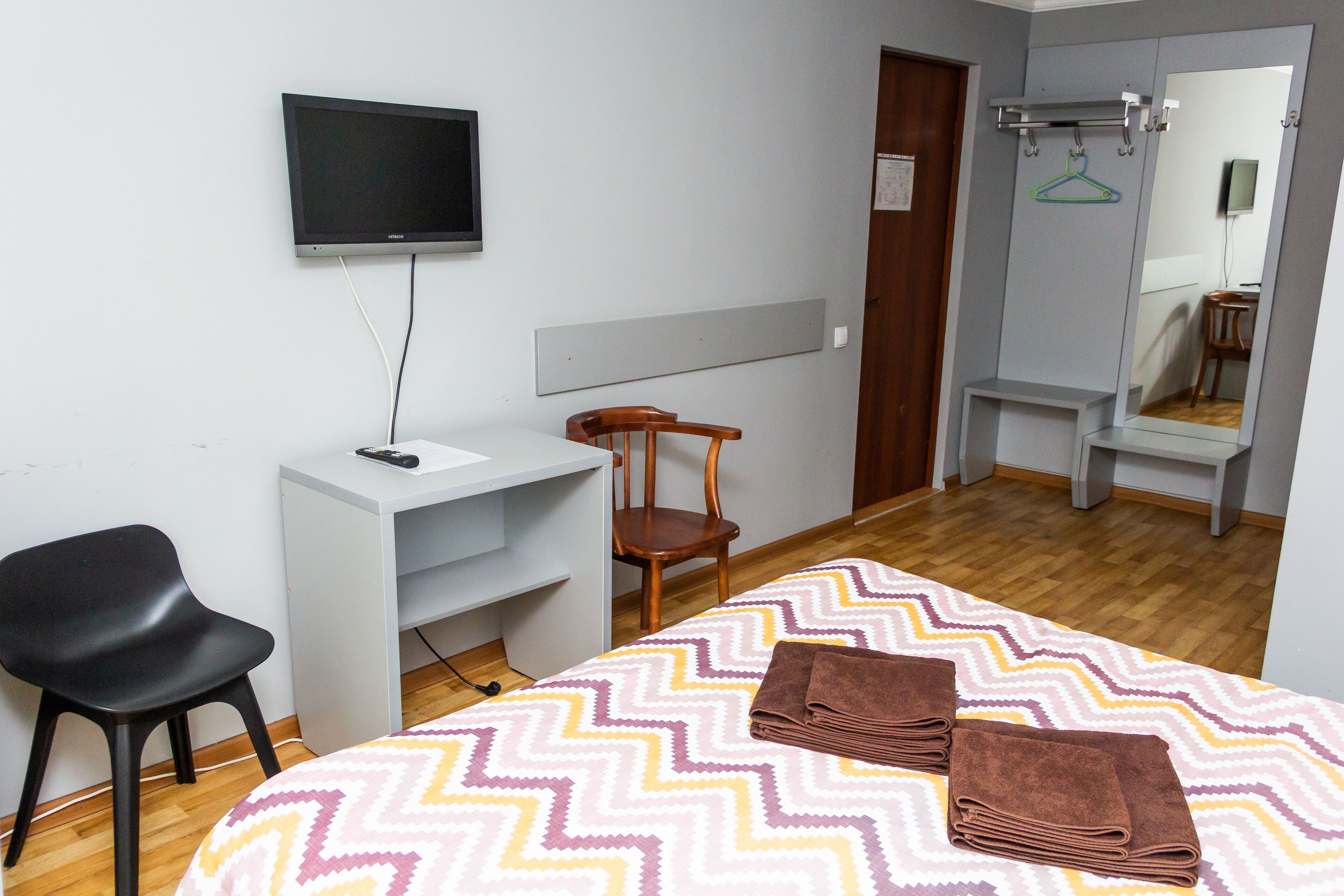 A hotel room with a bed, a desk, a chair, a TV, a mirror, and a wardrobe.