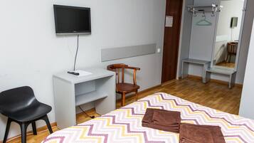 Een hotelkamer met een bed, bureau, stoel, televisie, spiegel en kledingkast.