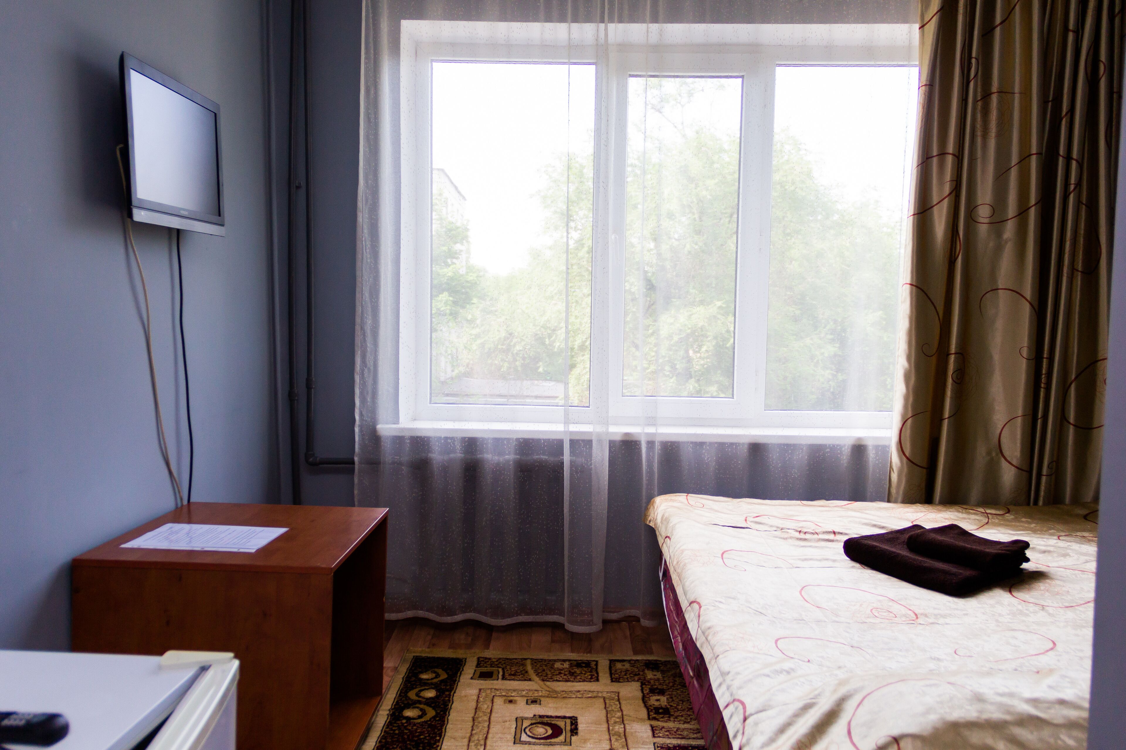 A hotel room with a bed, a desk, a television mounted on the wall, and a window with curtains.