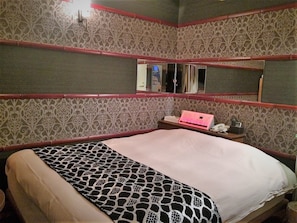 A room with a bed, a desk with a computer, and a mirror on the wall.