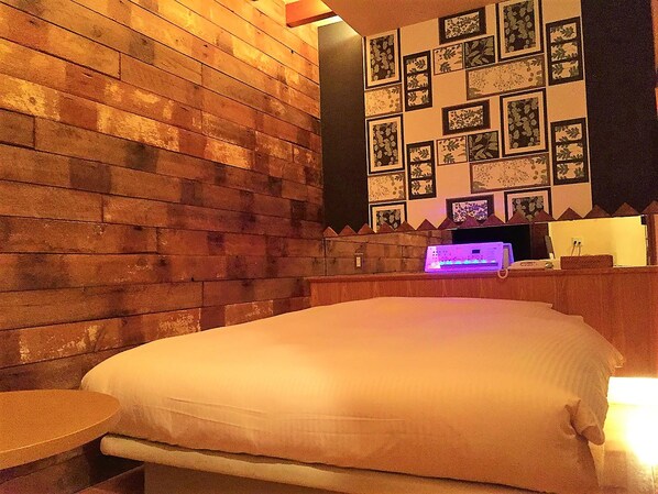 A room with a wooden wall, a bed, a small table, and a wall-mounted TV. - Hotel C-Heaven - Adults Only (Tokyo)