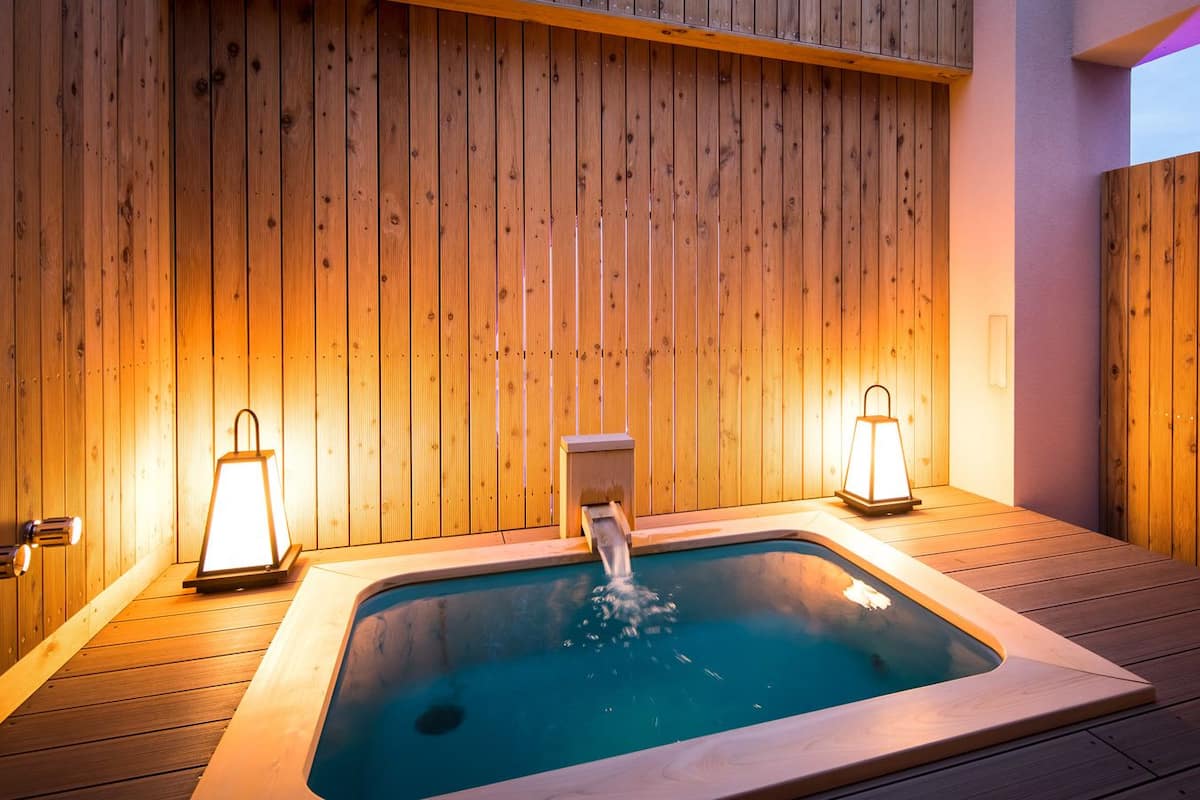 A hot tub with a wooden deck and two wall-mounted lanterns.