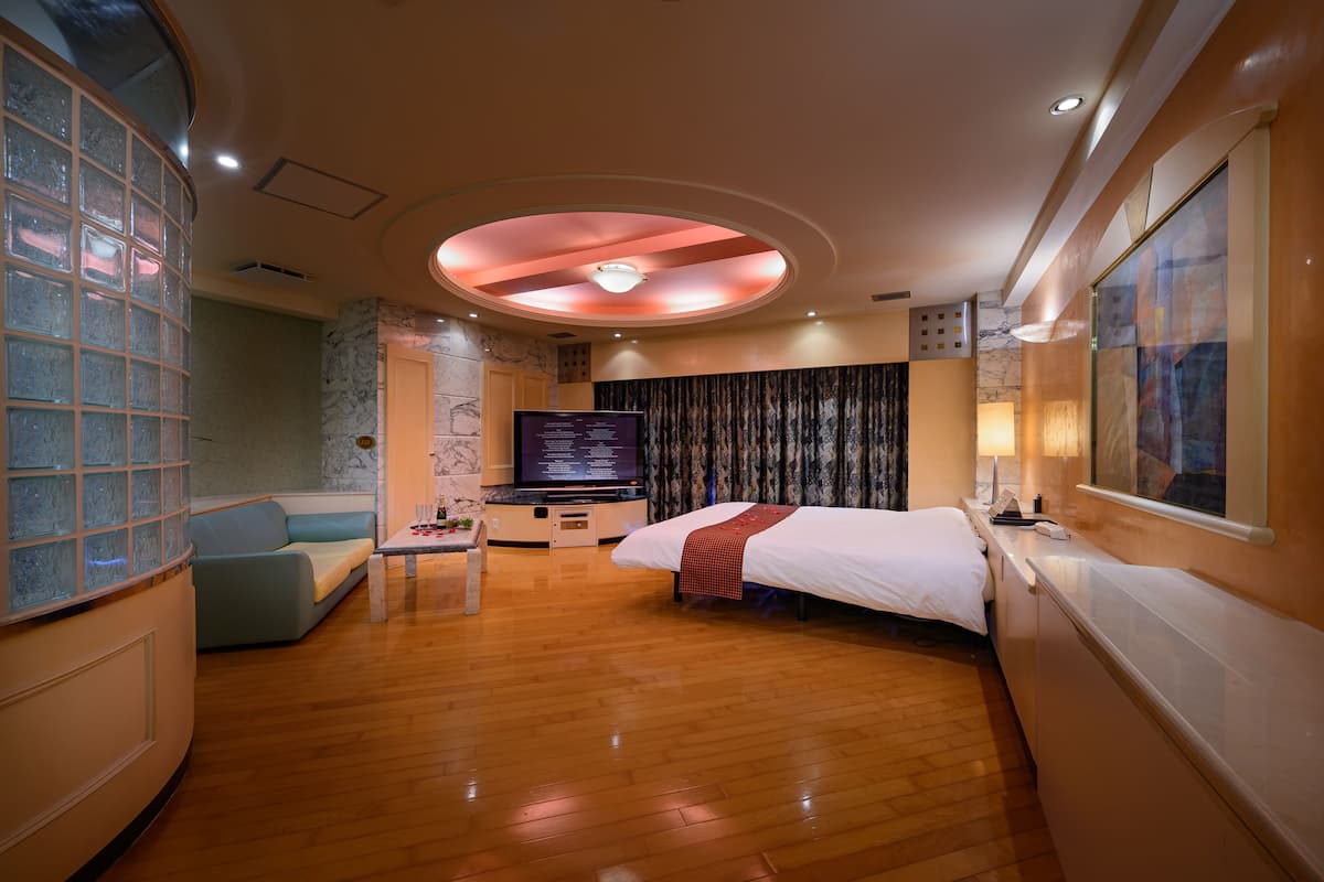A hotel room with a bed, a TV, a seating area, and a large window.