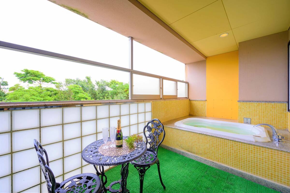 A balcony with a table, chairs, a bottle of champagne, and a bathtub.