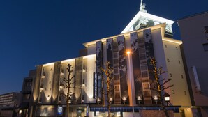 A modern hotel with a prominent entrance, large windows, and a flag indicating it is a New York Times building. - Hotel New York - Adults Only (Yokohama)