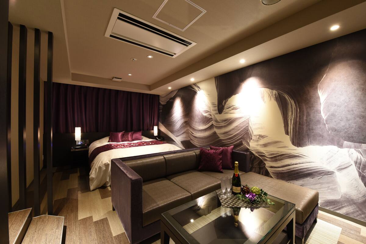 Une chambre d’hôtel moderne avec un grand lit, un canapé, une table basse en verre et une fresque murale.