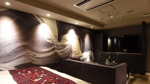 A modern hotel room with a large bed, a dark-colored sofa, a flat-screen TV, and a decorative wall mural. - Hotel New York - Adults Only (Yokohama)