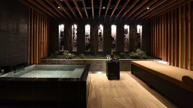 A modern spa area with a glass-enclosed hot tub, wooden ceiling beams, and a seating area with a bottle of champagne. - Hotel New York - Adults Only (Yokohama)