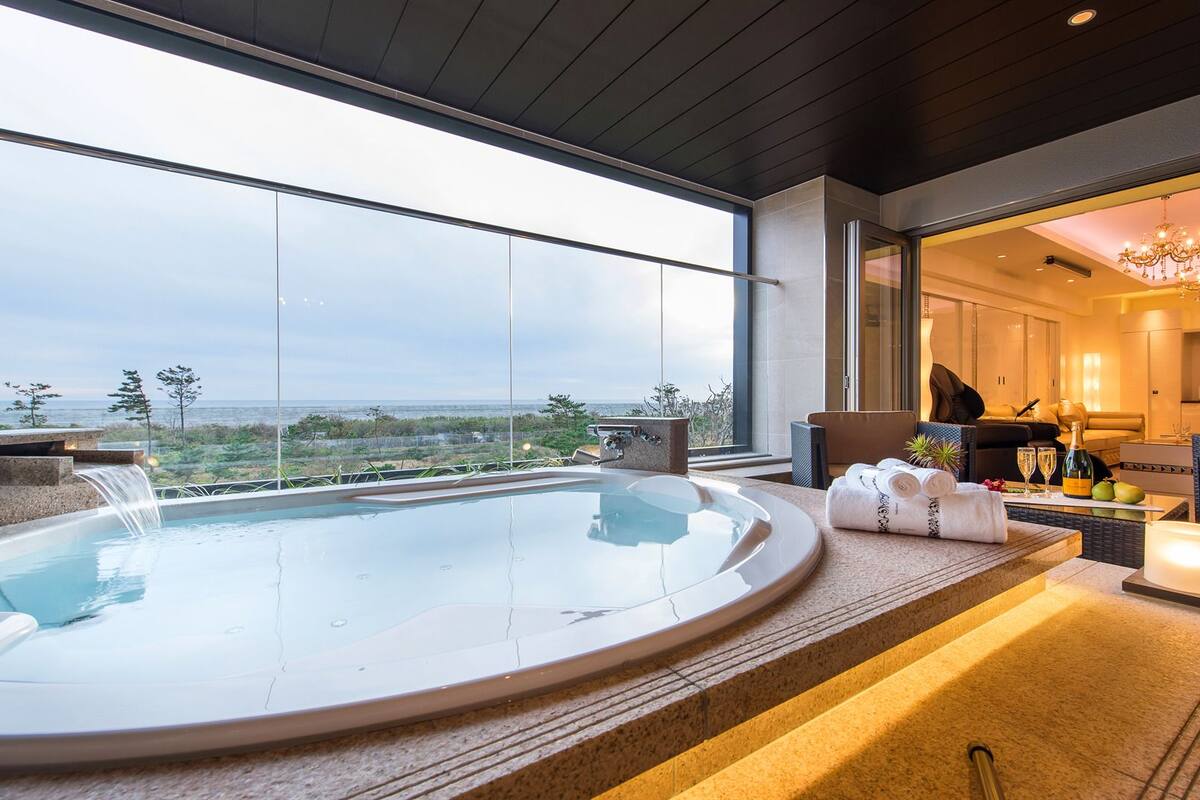 Ein moderner Wellnessbereich mit Whirlpool, Sitzgelegenheiten und Meerblick.