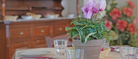 Een eettafel gedekt met borden, glazen en een potplant met roze bloemen.