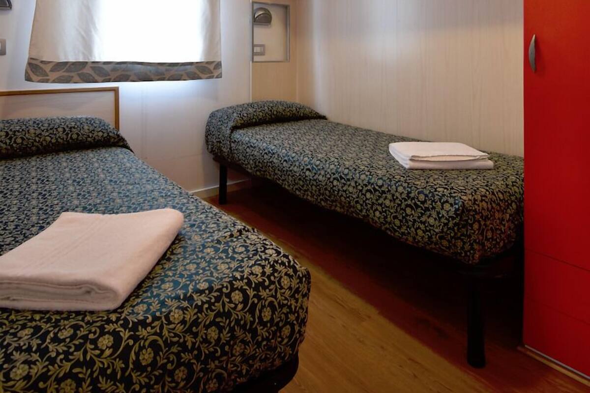 A room with two beds, a red wardrobe, a window with a curtain, and a ceiling light.
