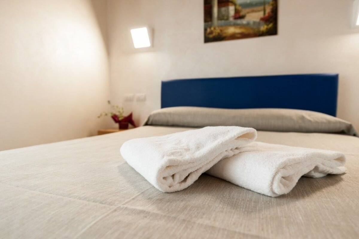 A neatly made bed with a folded white towel and a blue headboard.