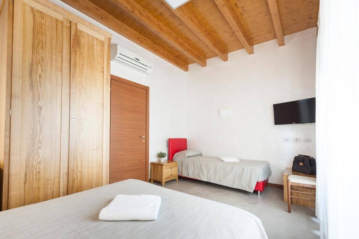 A bedroom with a wooden wardrobe, a bed with a red headboard, a bedside table with a lamp, and a TV mounted on the wall.