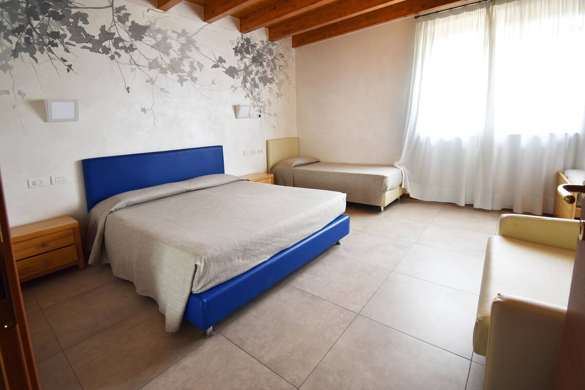 A bedroom with a large bed, a smaller bed, a wooden nightstand, a bedside table, and a window with curtains.