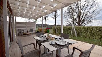 A covered outdoor dining area with a table set for four, surrounded by chairs, and a view of the countryside.