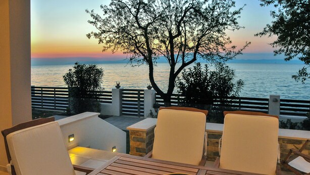 A terrace with two chairs and a table, overlooking a sunset over the sea.