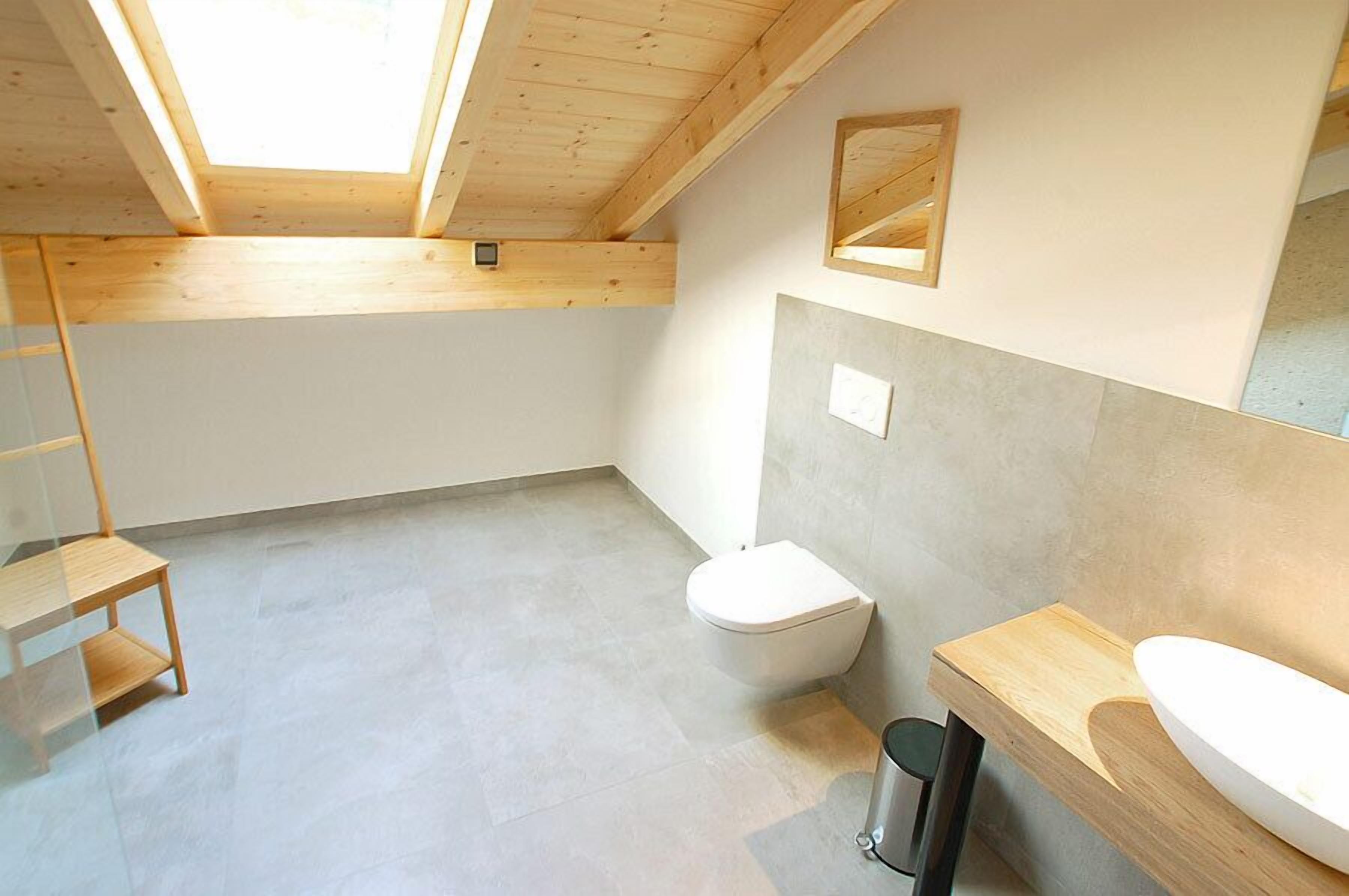 A modern bathroom with a skylight, a toilet, a sink, and a small wooden shelf.