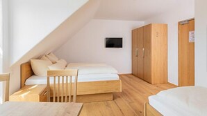 A bedroom with a sloped ceiling, a bed, a wooden wardrobe, a desk, and a chair. - Gästehaus Neubauer (Althegnenberg)