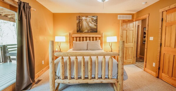 Un dormitorio con estructura de cama de madera, dos lámparas de noche, un cuadro en la pared y una puerta de madera.