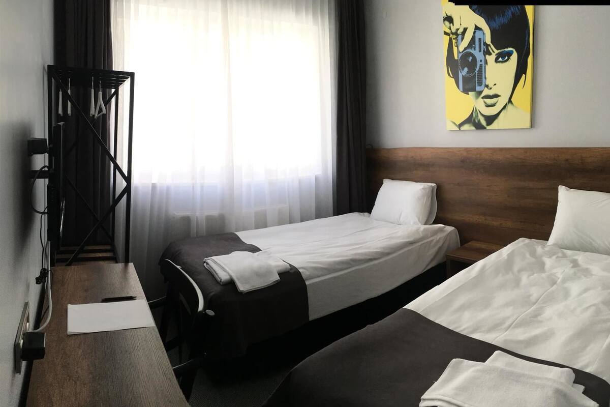 A hotel room with two beds, a wooden headboard, a desk with a chair, a mirror, and a painting on the wall.