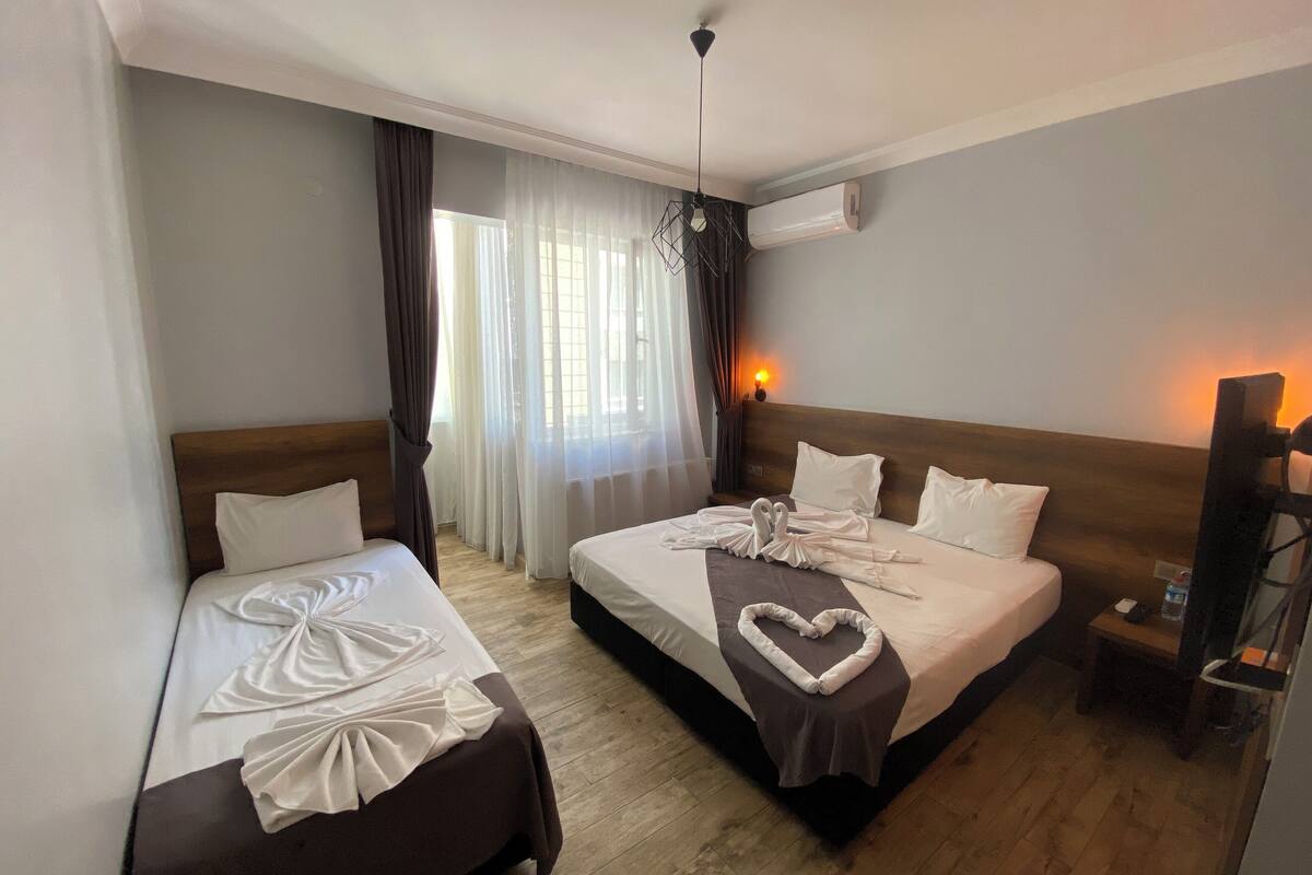 A hotel room with two beds, a ceiling fan, an air conditioning unit, and a window with curtains.